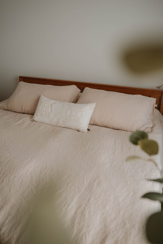 un décor d'oreillers de couleur neutre sur un lit king entouré de feuilles d'eucalyptus
