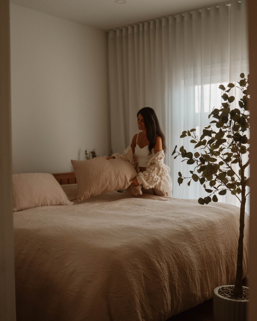 femme en pyjamas en train de faire son lit dans une ambiance neutre et paisible d'une chambre à coucher